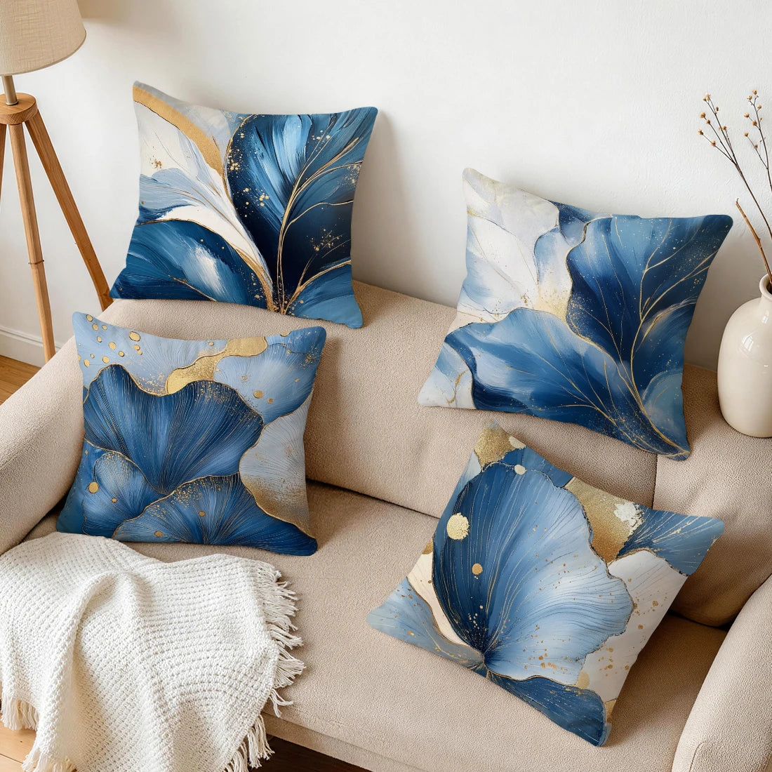 A collection of abstract leaf print cushions in shades of blue, white, and gold on a beige sofa.