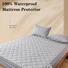 A gray waterproof mattress protector is shown on a bed, folded and displayed next to a pillow.