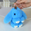 A fluffy light blue bunny keychain with a pom pom tail is being held by a hand.
