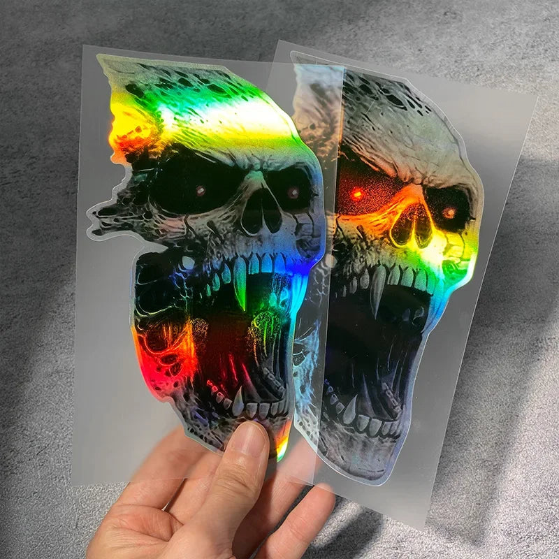A hand holds a waterproof vinyl skull decal featuring a vibrant rainbow gradient of colors.