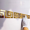 Gold acrylic mirror wall stickers in a repeating Greek key pattern mounted on a white surface.