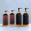 A set of three black and wood refillable soap dispensers with black pump tops on a light blue surface.