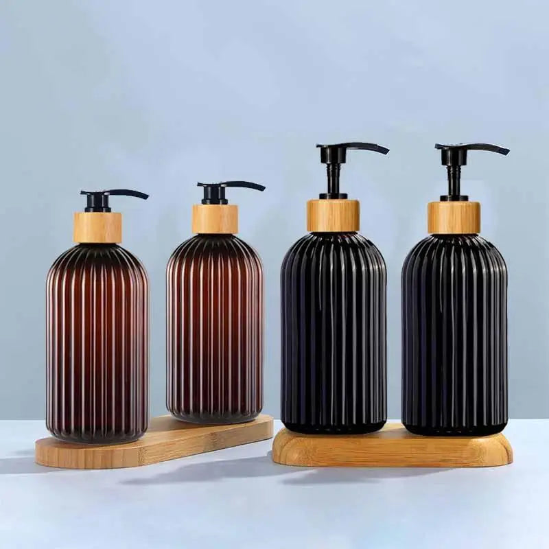 A set of three black and wood refillable soap dispensers with black pump tops on a light blue surface.