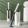 A white disposable toilet cleaning brush with a black handle and storage base is shown against a green background.