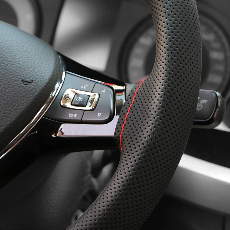 Close-up of a black Napa leather steering wheel cover with silver buttons and red stitching on a car interior.