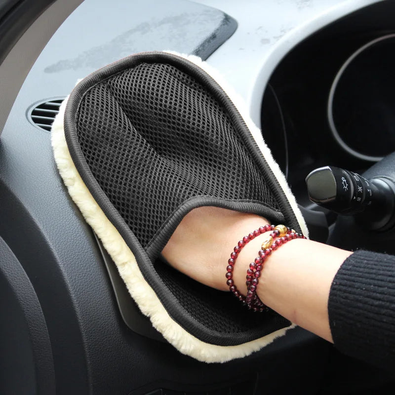 A hand wearing a red beaded bracelet rests on a black microfiber car wash glove inside a car interior.