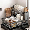 A black two-tier kitchen countertop drying rack holding stacks of white and brown plates and cutlery.