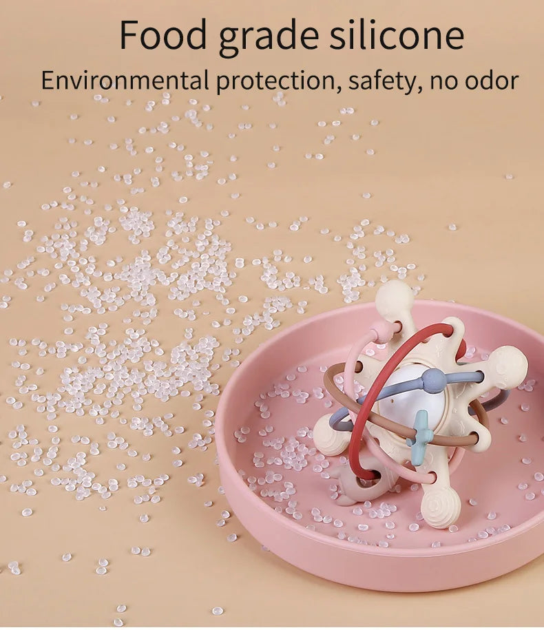 A pink silicone sensory rattle ball for baby development is shown on a light pink plate with scattered silicone pieces.