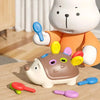 Ein weißer Teddybär hält ein braunes Igel-Sensorspielzeug mit farbigen Stäbchen und Ringen auf einer Holzoberfläche.