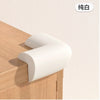 A white soft baby corner guard is shown placed on a wooden cabinet surface.