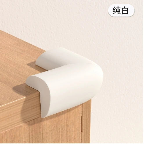 A white soft baby corner guard is shown placed on a wooden cabinet surface.