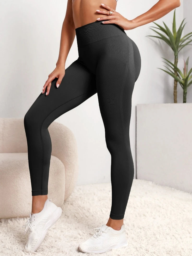 A model wearing black high-waist sculpting leggings and white sneakers, standing indoors.