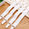 A set of four white adjustable bed sheet holder clips lying on a wooden surface next to a beige towel.