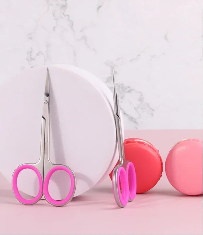 A pair of professional stainless steel cuticle scissors with curved blades resting on a pink surface.