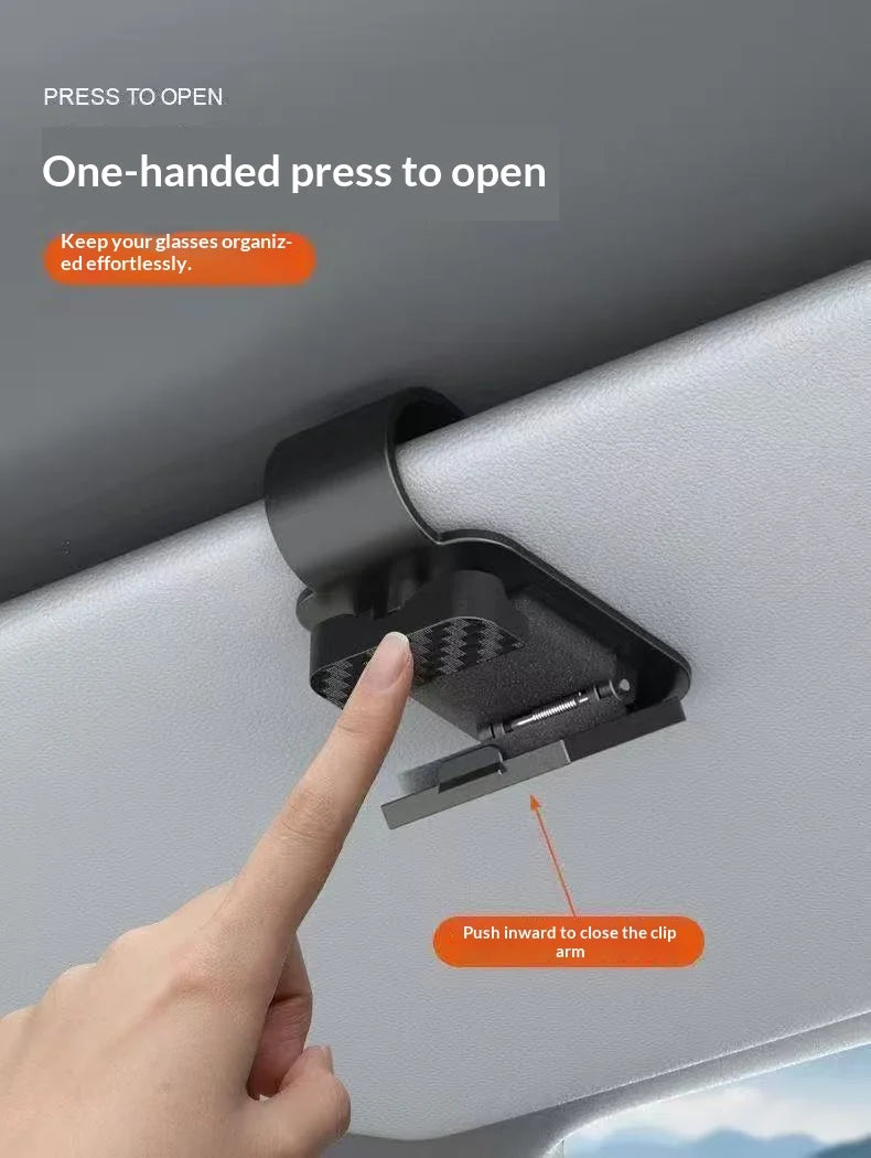 A hand is pressing a one-handed press to open mechanism on a car sunshade magnetic glasses holder.