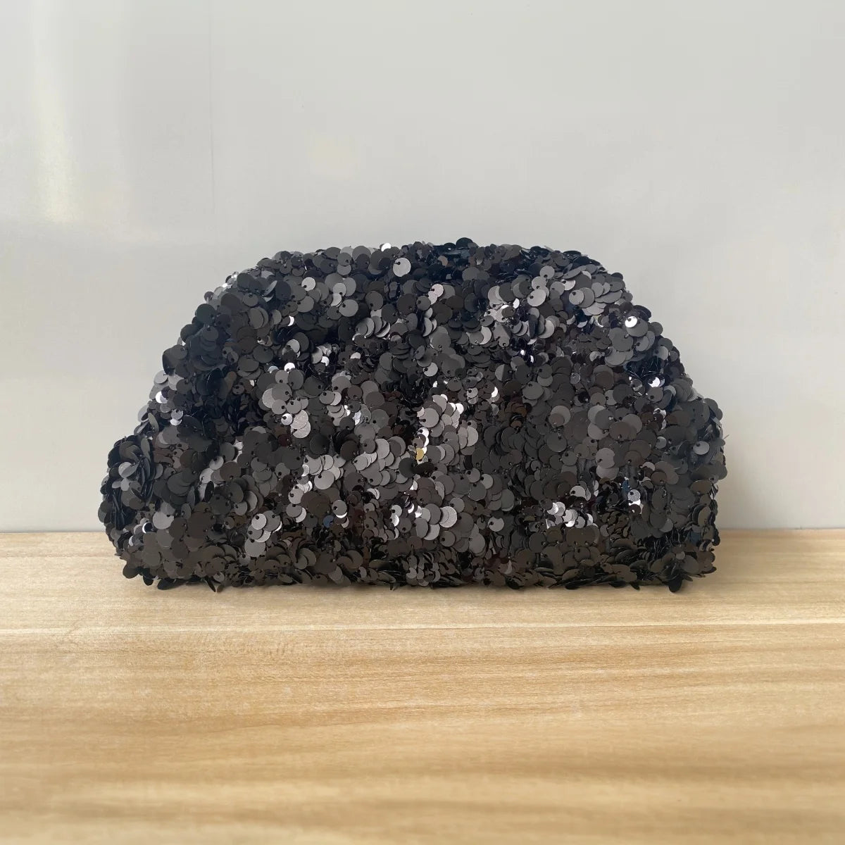 A black sequin beaded chain shoulder clutch bag resting on a light wooden surface.