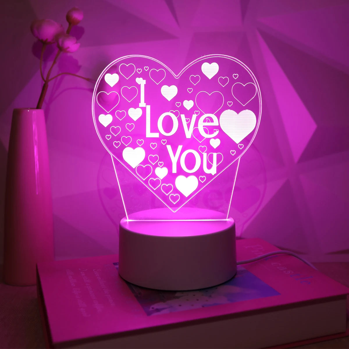 A pink LED heart night light with a glowing 'I Love You' design illuminates a surface.