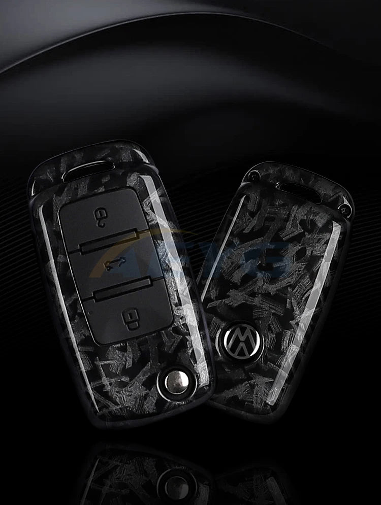 A pair of black carbon fiber car key covers for VW and Skoda models displayed on a dark surface.