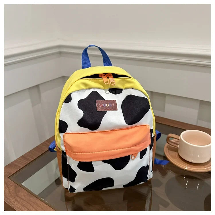 A yellow and black cow print backpack with blue straps resting on a wooden surface.