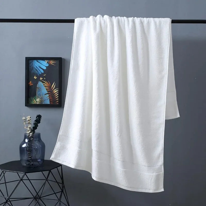 A white premium pure cotton bath towel hanging on a rack against a gray wall.