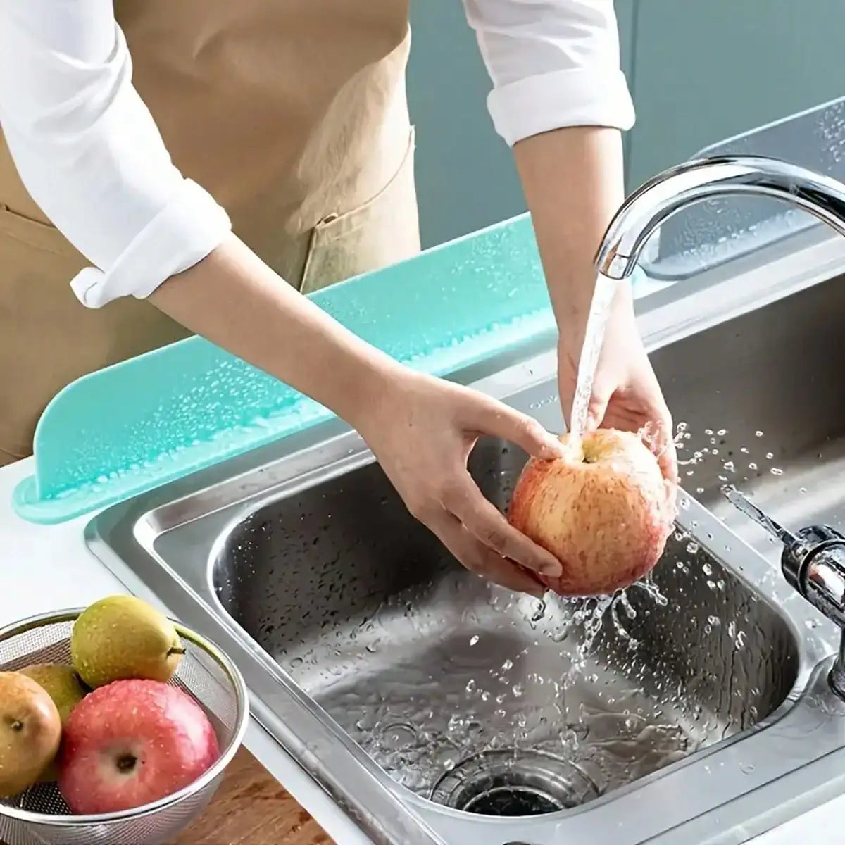 Eine Hand benutzt einen Silikon-Spritschutz mit Saugnapf, um einen Apfel in einer Edelstahlspüle zu waschen.