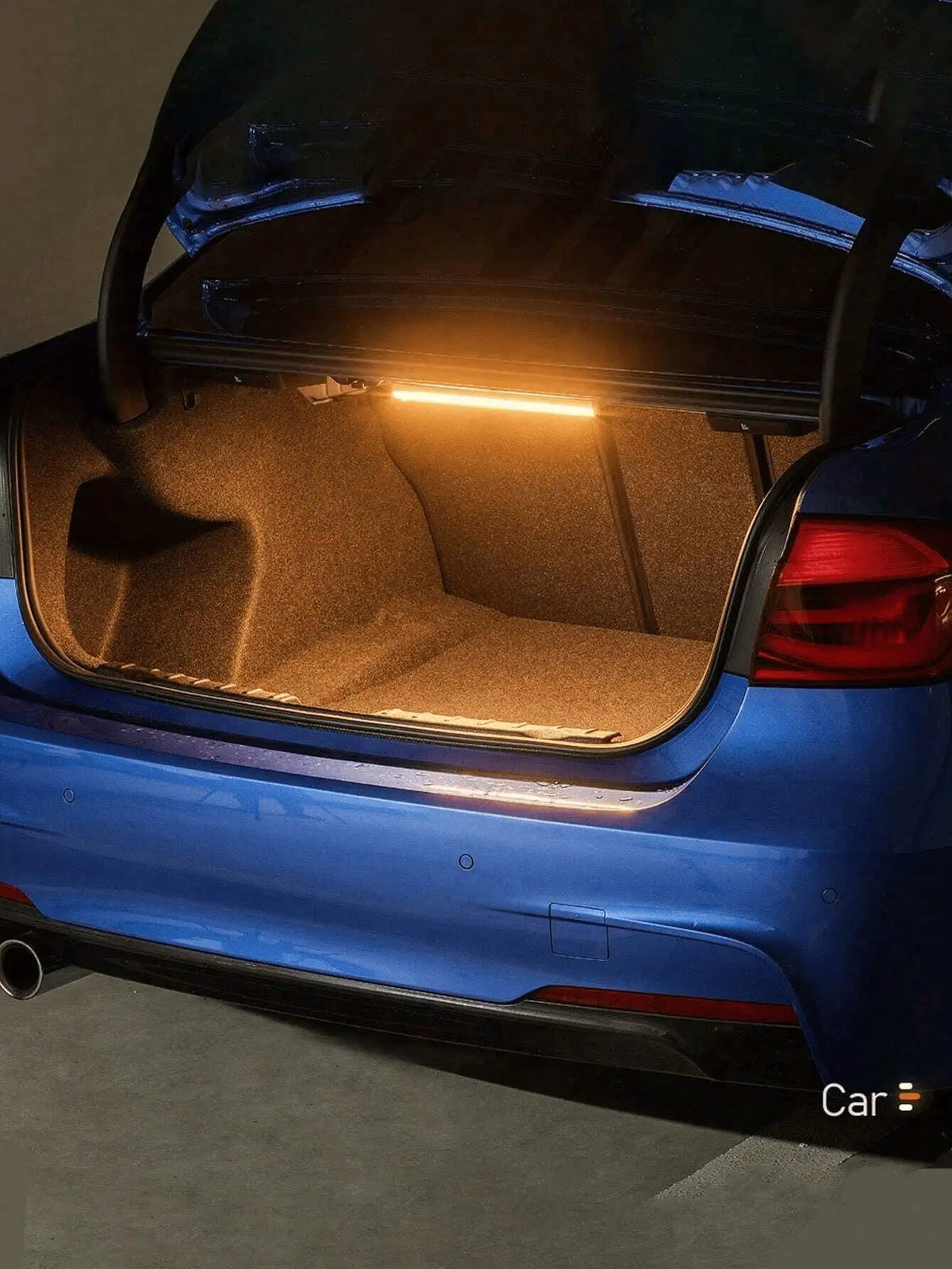 Rear view of a blue car showing an illuminated LED light inside the trunk.