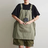A person wearing a olive green waterproof work apron over a black shirt and khaki shorts.