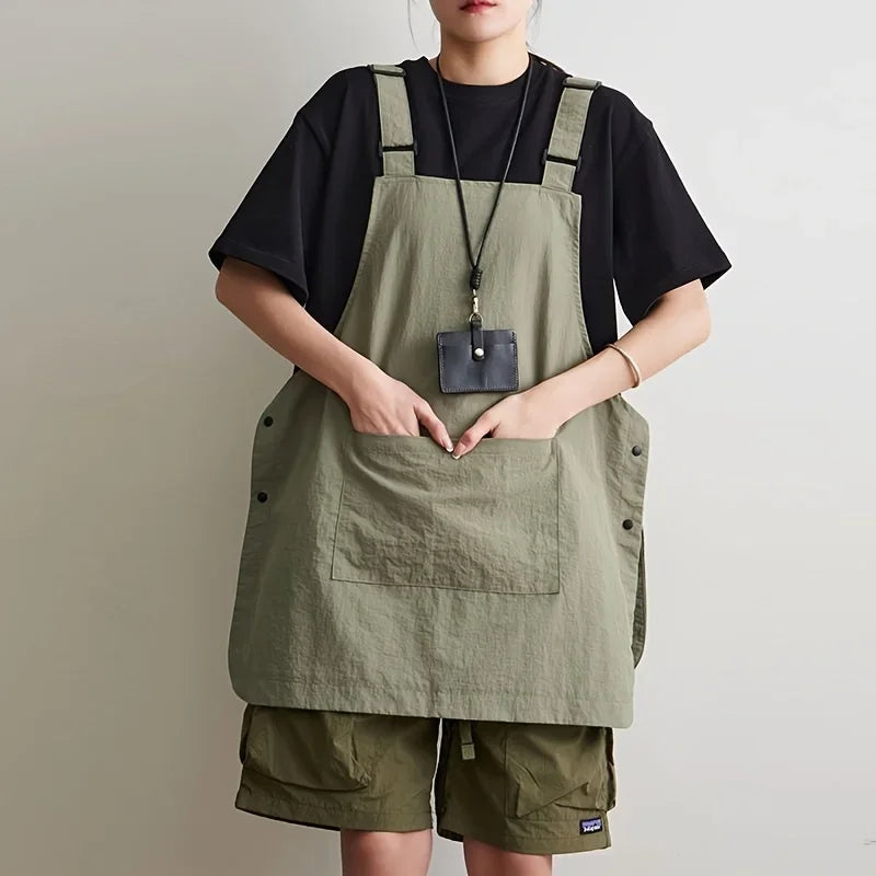 A person wearing a olive green waterproof work apron over a black shirt and khaki shorts.