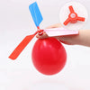 A hand holds a red balloon with an attached propeller and whistle toy.