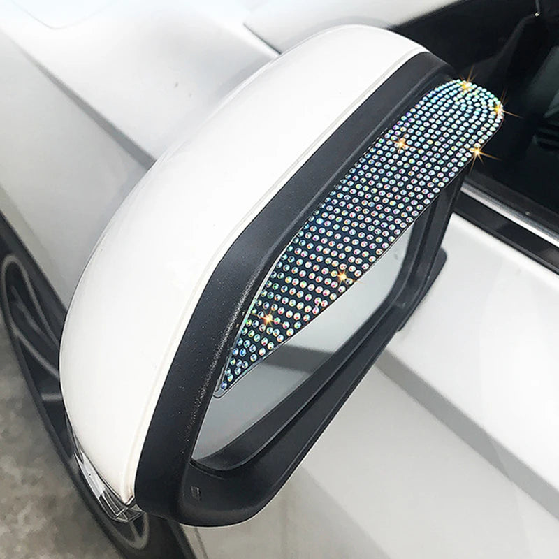 A white car rearview mirror with a clear lens and a decorative rhinestone rain guard covering the top edge.