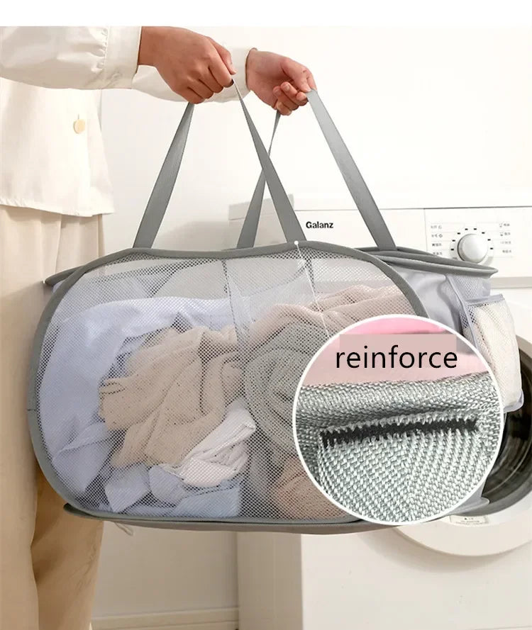 A person is holding a gray folding mesh laundry basket with handles, showing the interior filled with folded clothes.