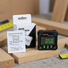 A black digital inclinometer device is shown next to its instruction manual and a wooden block.