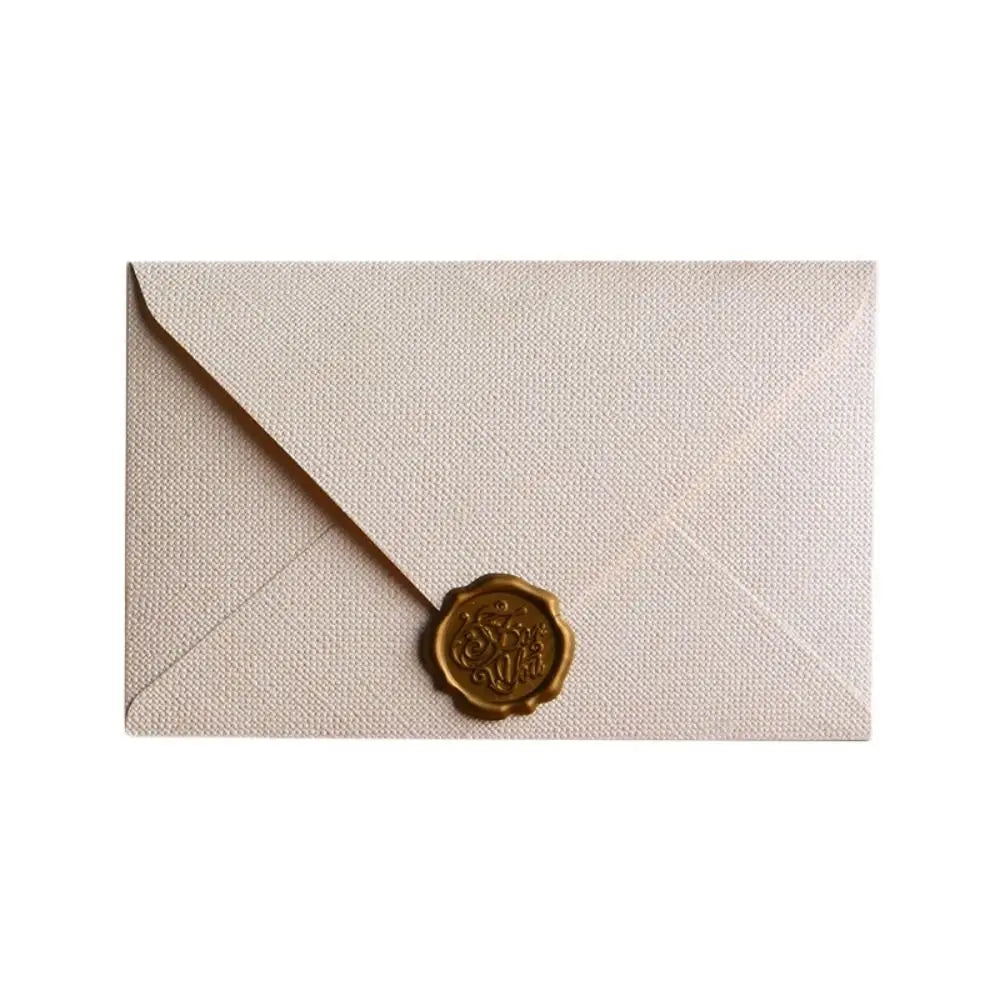 A pale beige linen texture envelope with a gold sealing wax sticker on the front.