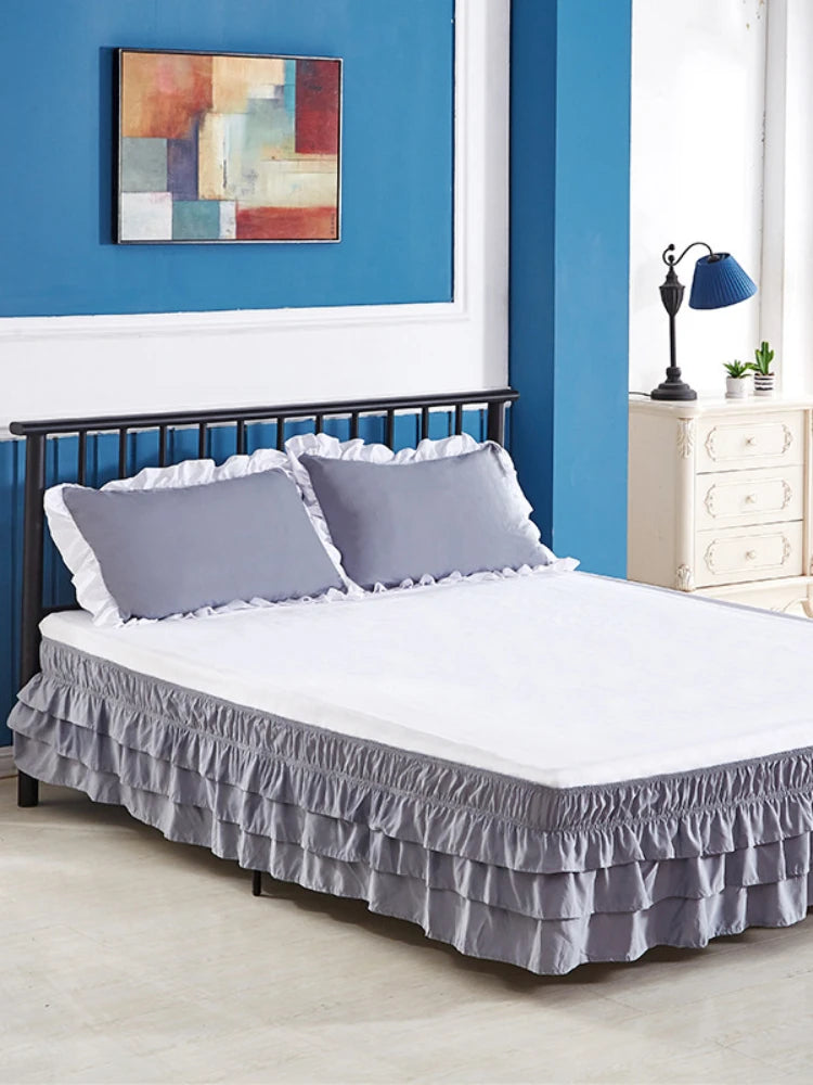 A bed with a gray elastic skirt and white bedding against a blue wall.