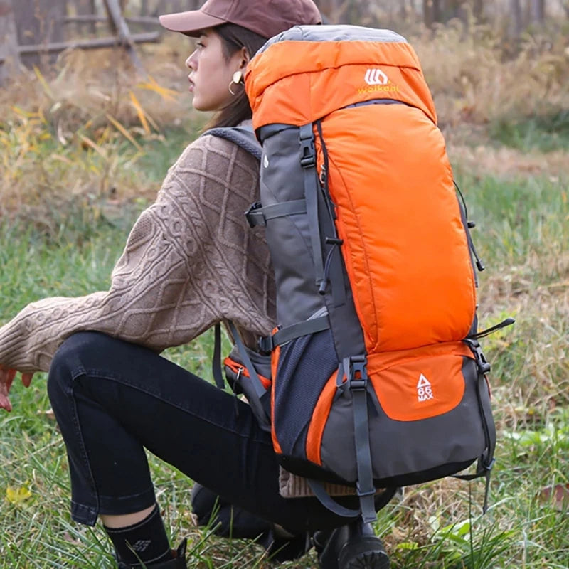 A woman wearing a brown sweater is sitting outdoors with an orange and gray waterproof hiking backpack.