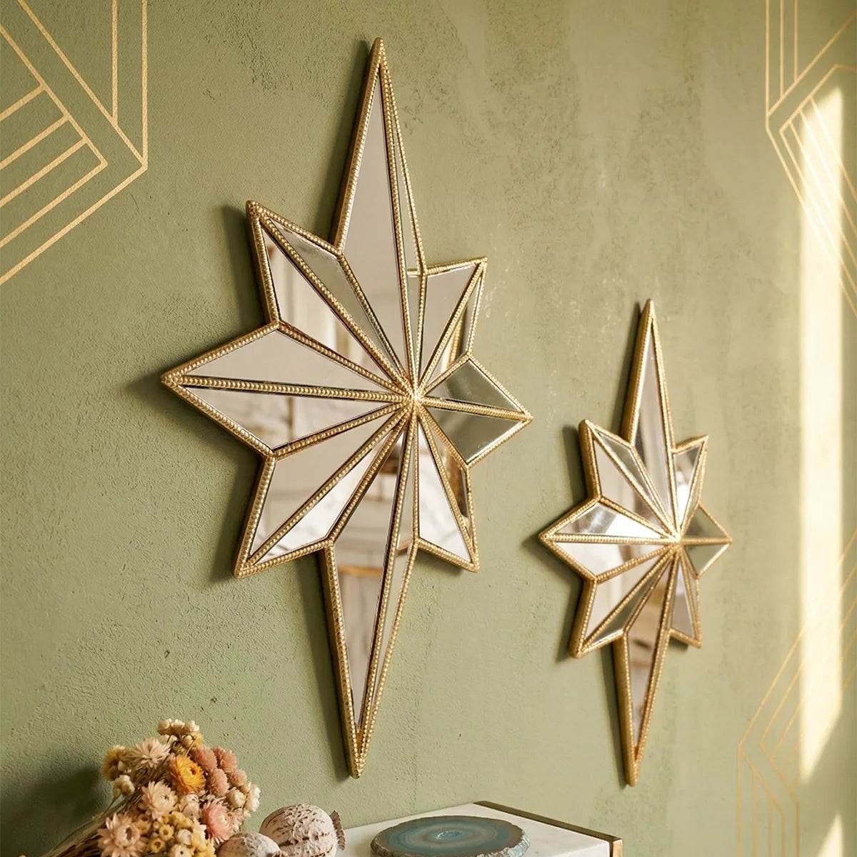 A gold-framed octagonal star resin wall mirror mounted on a muted green textured wall.