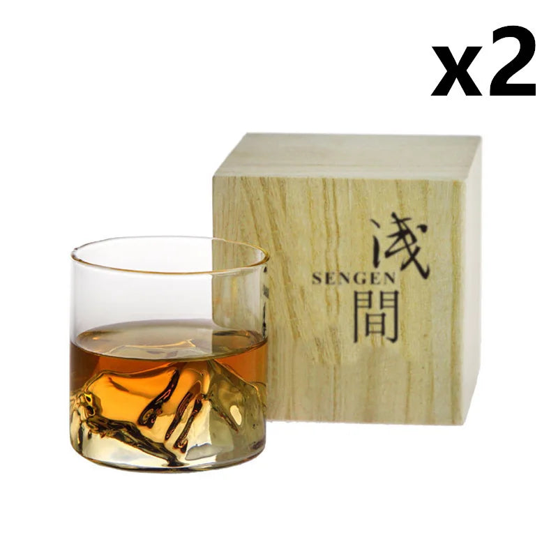 A clear whiskey glass sits next to a light wooden box with Japanese text on it.