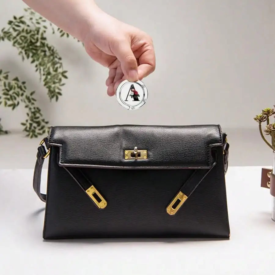 Eine schwarze Lederclutch mit goldenen Verzierungen wird über einem personalisierten Briefhaken gehalten.