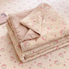 A stack of light pink cartoon pattern kids lightweight summer quilts lying on a textured white surface.