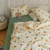 A light yellow bedding set with a white duvet cover and pillows featuring an orange and green floral pattern.