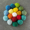 A collection of brightly colored, hand-spun yarn balls in various shades of blue, green, yellow, and orange scattered on a gr