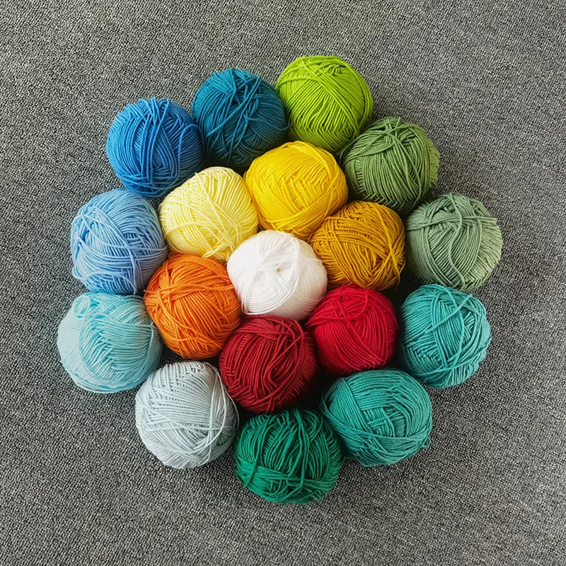 A collection of brightly colored, hand-spun yarn balls in various shades of blue, green, yellow, and orange scattered on a gr