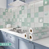 A kitchen splashback featuring light green square tiles and gray cabinetry with rolls of self-adhesive wallpaper.