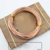 A coil of rose gold anodized aluminum jewelry wire resting on a wooden board.