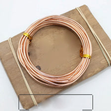 A coil of rose gold anodized aluminum jewelry wire resting on a wooden board.
