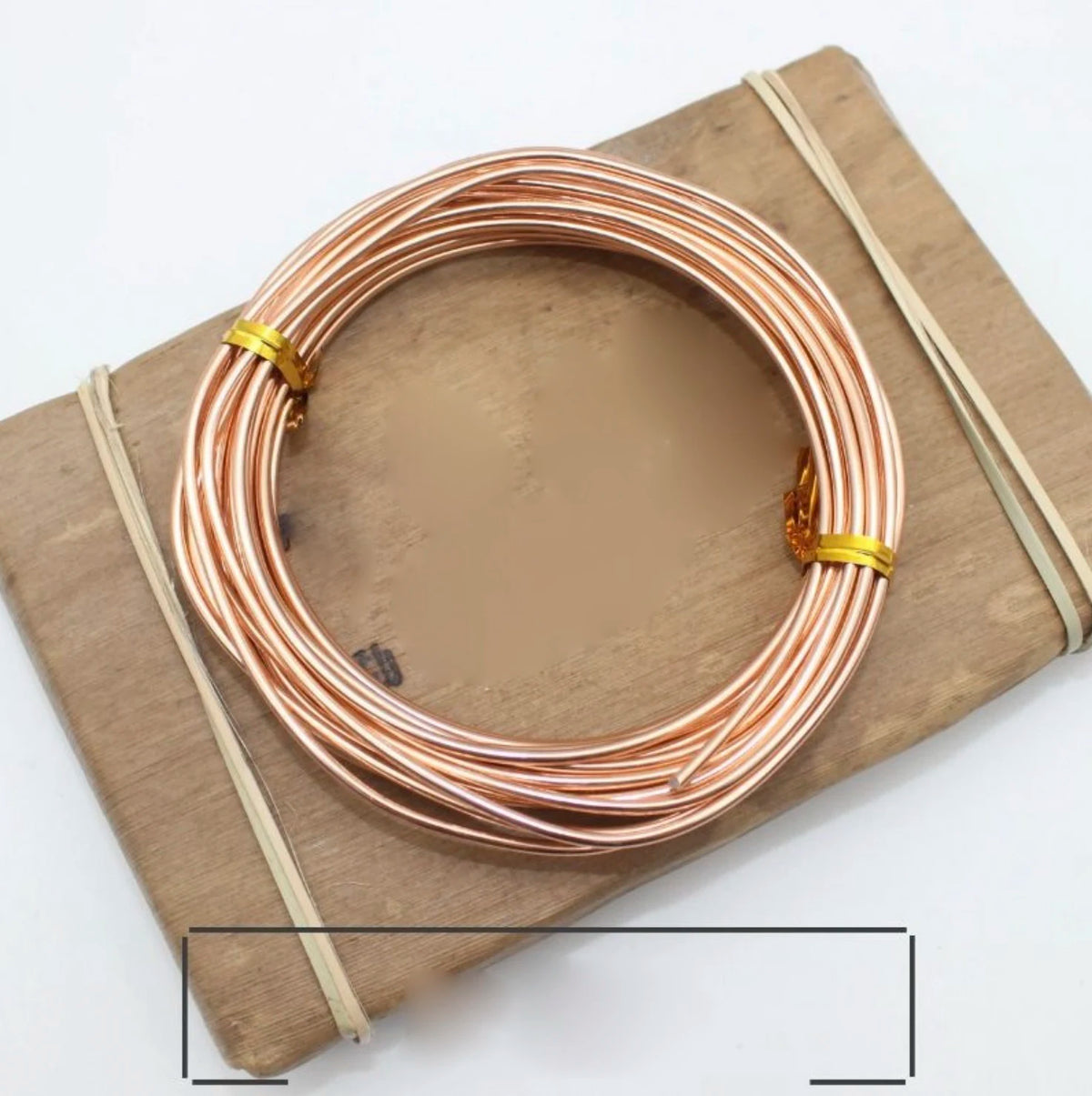 A coil of rose gold anodized aluminum jewelry wire resting on a wooden board.