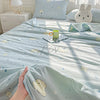 A light blue quilt with a pastoral print featuring small white animals and stars, displayed on a bed.