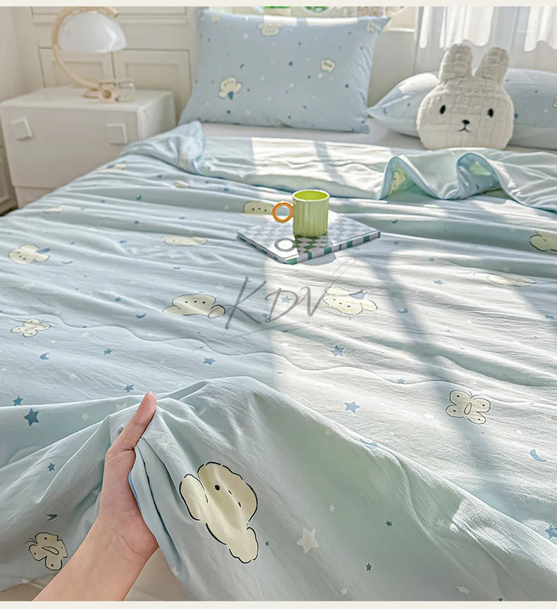 A light blue quilt with a pastoral print featuring small white animals and stars, displayed on a bed.