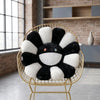 A black and white sunflower plush cushion with a smiling face is displayed in a gold wire chair.