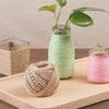 A glass jar filled with green twine and a bundle of natural jute twine on a wooden board.